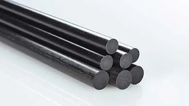 Close-up of black carbon fiber rods stacked on a white, reflective surface.
